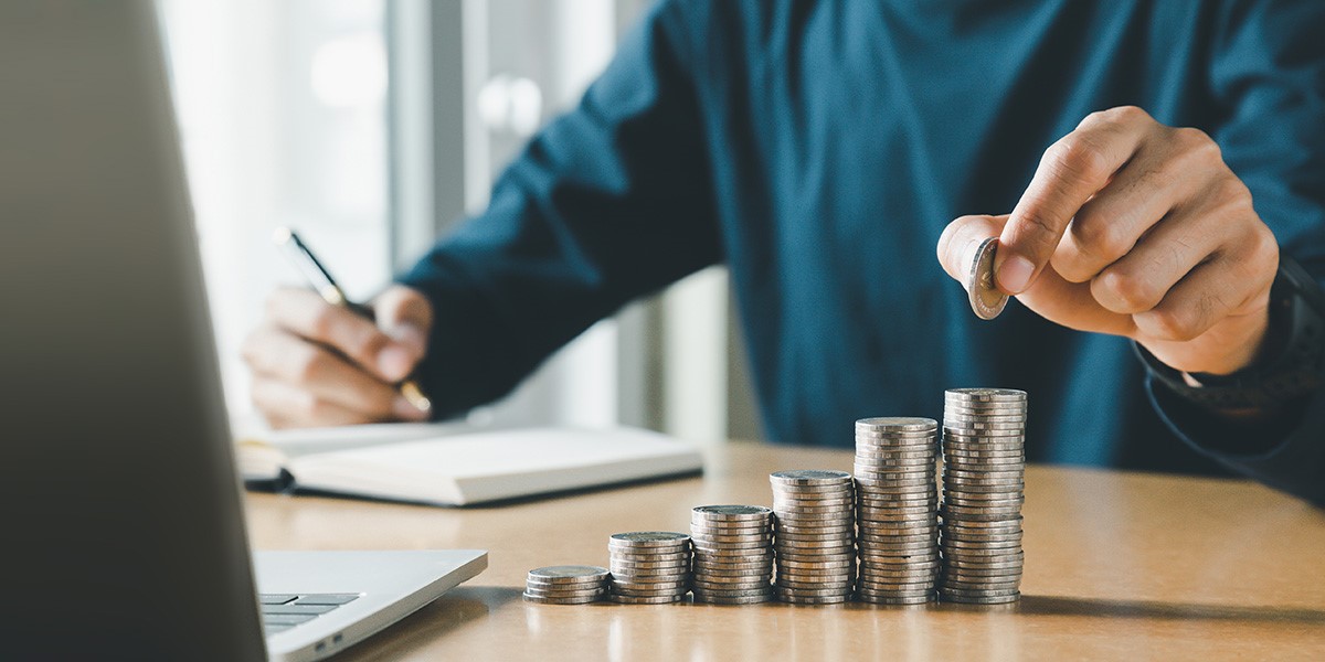man making notes on how much money he has with coins stacked on one another