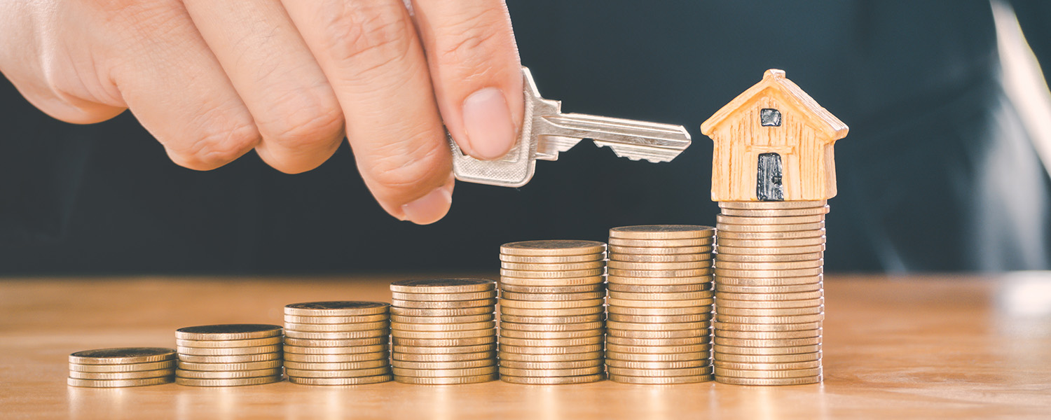 Stack of coins lined up with house on tallest stack, a key being pointed at the house