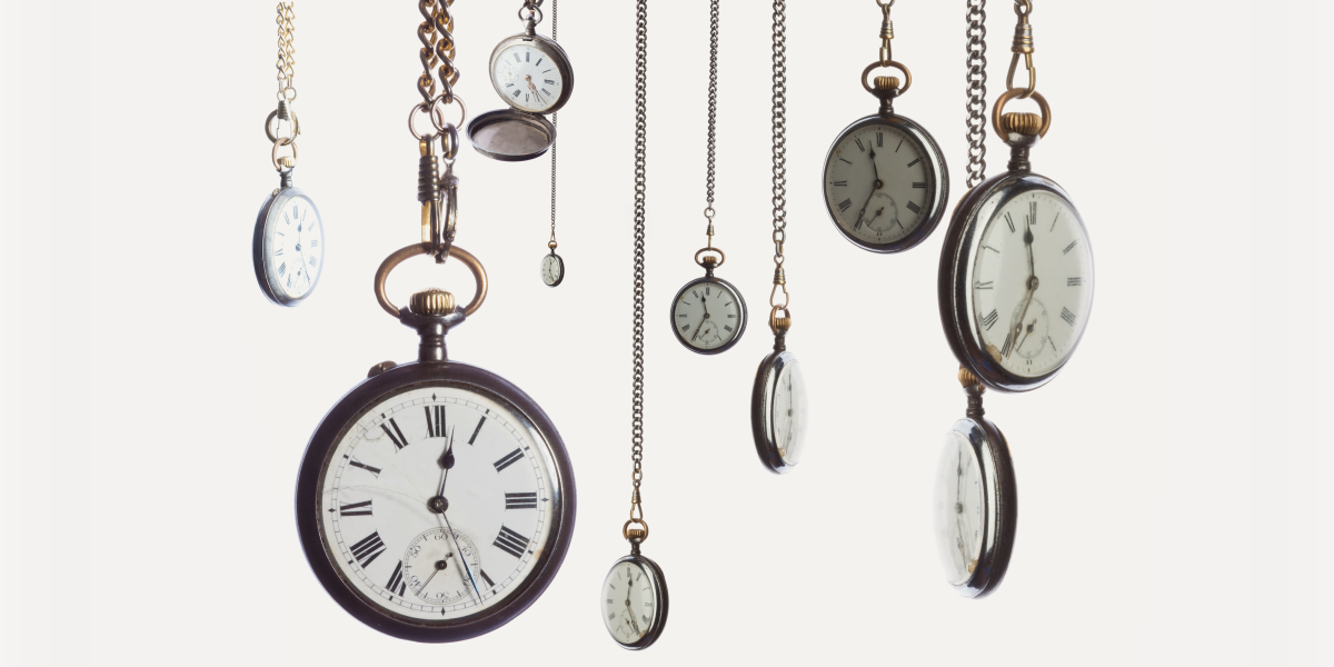 A collection of vintage pocket watches hanging from thin chains against a light background, showcasing various styles and sizes.